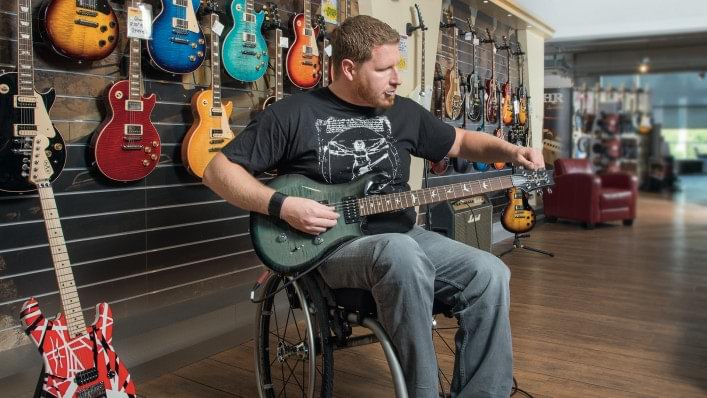 Un homme en fauteuil roulant accorde une guitare