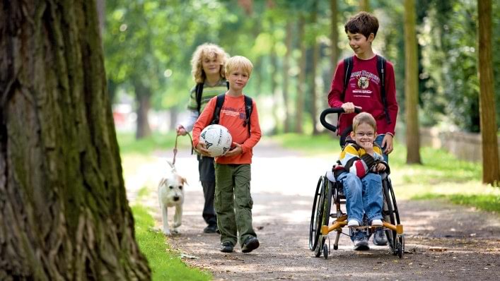 Un enfant en fauteuil roulant, en promenade avec des amis